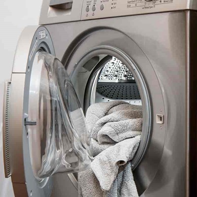 En sølvfarvet vaskemaskine. Der ligger et håndklæde i maskinen, som lågen ikke er lukket på endnu.